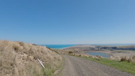 POV-Off-Road-downhill-cycling-with-incredible-views-of-lake-and-ocean-on-a-summer's-day---Bossu-Road,-Canterbury