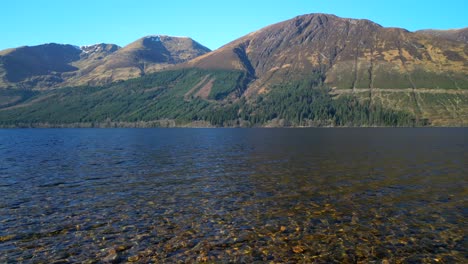 Low-slow-flight-over-shoreline-clear-water-of-Loch-Lochy-Scottish-Highlands