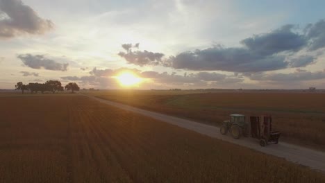 Farmer-driving-large-industrial-commercial-farm-equipment-along-dirt-road-at-sunrise