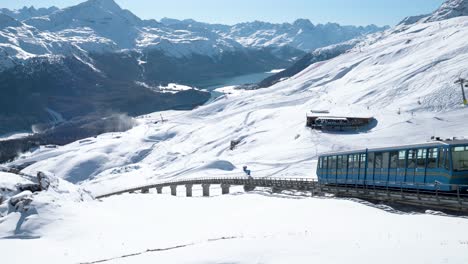 Blue-cable-car-going-down-surrounded-by-snowy-winter-landscape-and-mountains-in-St