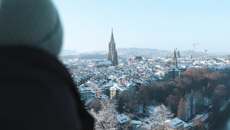 Man-looking-at-the-view-of-the-snow-covered-old-town-and-cathedral-in-Bern,-Switzerland-during-winter