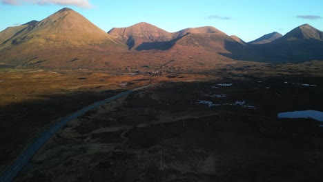 Elevating-shot-revealing-highland-road-and-Red-Cuillin-mountains-lit-by-sunrise-at-Sligachan-on-the-Isle-of-Skye-Scotland