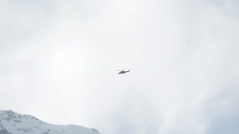 Helicopter-flying-through-clouds-and-over-snow-covered-mountain-peaks-during-winter