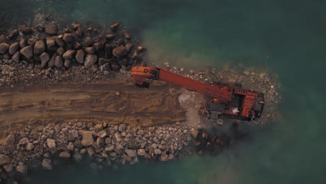 Construction-of-a-new-breakwater-at-sea-by-Excavator-machine,-top-down-to-pullback-reveal-view