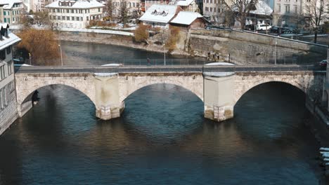 Auto-Fährt-Auf-Einer-Alten-Steinbrücke-Vorbei,-Während-Im-Winter-In-Bern,-Schweiz,-Wasser-Fließt