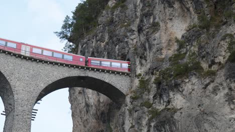 Traditioneller-Roter-Schweizer-Panoramazug,-Der-Auf-Einem-Steinbrückenviadukt-In-Einen-Gebirgstunnel-In-Der-Landwasserbrücke-Fährt