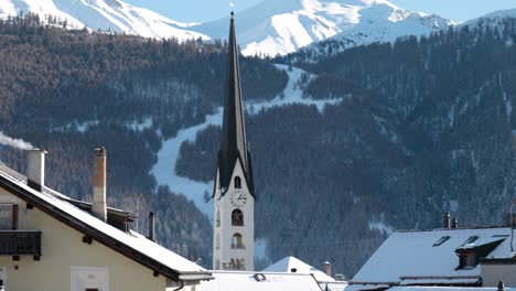 View-of-a-church,-mountains-and-houses-in-a-traditional-Swiss-village-of-Zuoz,-Switzerland-during-winter