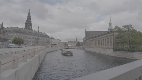 Christianborg-Gebäude-In-Kopenhagen-Weitblick-über-Den-Fluss,-Während-Ein-Boot-An-Einem-Bewölkten-Tag-Vorbeifährt