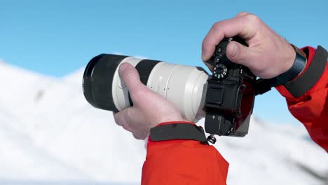 Detail-of-caucasian-male-hands-holding-up-a-camera-and-photographing-winter-snowy-mountain-landscape