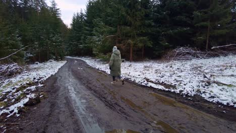 A-girl-dressed-in-a-warm-winter-jacket-is-walking-along-a-muddy-path-in-the-forest