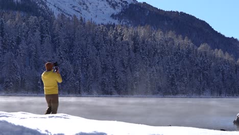 Caucasian-young-man-recording-a-video-with-a-camera-on-a-gimbal-next-to-snow-covered-lake-and-trees-in-St