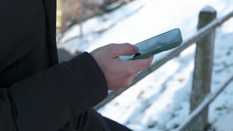Detail-view-of-a-caucasian-male-hand-scrolling-through-a-smartphone-while-outdoors-during-winter