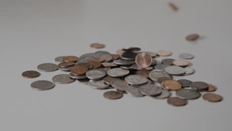 A-pile-of-change,-additional-coins-falling-into-frame-and-onto-the-pile-in-slow-motion