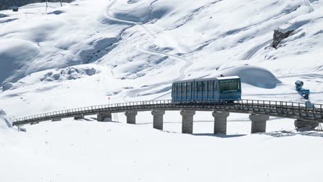 Blue-cable-car-going-down-surrounded-by-snowy-winter-landscape-and-mountains-in-St