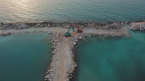 A-flat-sea-at-sunset-with-two-excavators-standing-on-a-stone-pier-they-built