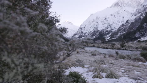 Reveal-shot-of-running-river-in-a-valley-surrounded-by-snow-capped-peaks-and-mountains-in-winter,-New-Zealand