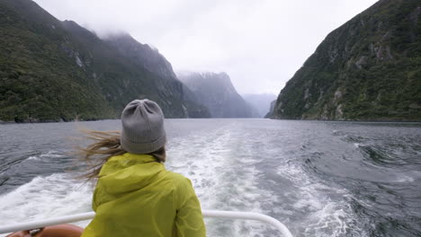 Slow-motion-shot-of-girl-in-yellow-rain-jacket-on-back-of-boat-surrounded-by-mountains-and-fiords
