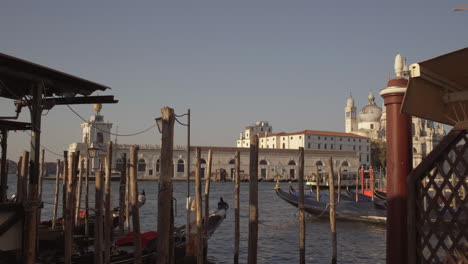 Wide-shot-of-gondolas-parked-in-pier-with-wooden-poles,-Venice,-Italy