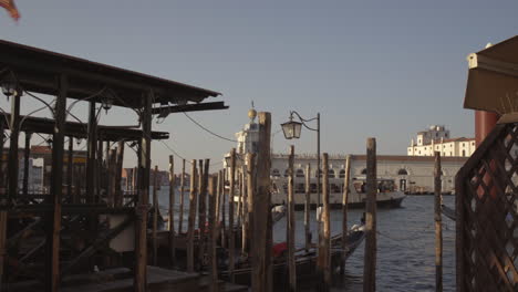 Dynamic-wide-shot-of-red-Venetian-Flag-in-wind-and-gondolas-parked-in-pier-with-wooden-poles