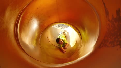 Little-boy-in-bright-green-shirt-tries-to-climb-back-up-yellow-tube-slide
