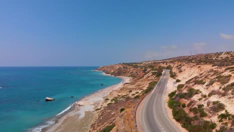 Aerial-drone-shot-rising-up-over-Paphos-Cyprus-as-cars-drive-along-a-seaside-road-near-Aphrodite's-Rock
