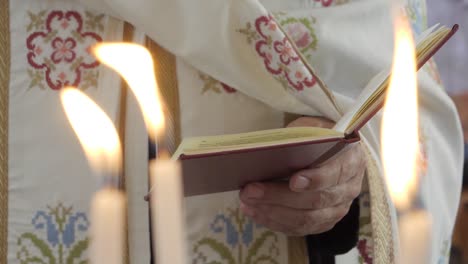 Close-up-of-a-priest's-hands-holding-religious-book-with-lit-candles-in-the-foreground