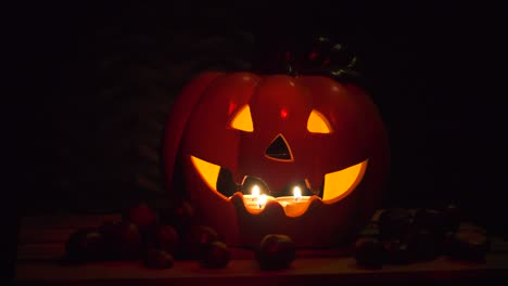 Halloween-Kürbis-Auf-Dunklem-Hintergrund-Mit-Kastanien,-Von-Kerzen-Beleuchtet,-Dunkelroter-Schein-Auf-Schwarz,-Isoliert-Mit-Copyspace,-Urlaubskonzept,-Dekoration,-Schwenk-Von-Links-Nach-Rechts,-Parallaxe