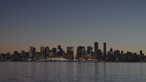 Vancouver-downtown-skyline-at-dusk,-birds-flying-over-water