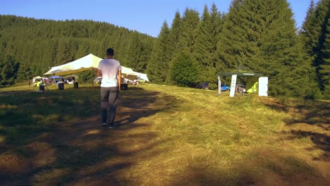 Tracking-Shot-Following-a-Young-Adult-Male-Millennial-Walking-Down-a-Path-at-a-Romanian-Festival-in-the-Mountains