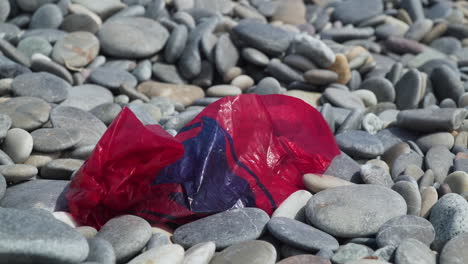 Red-plastic-bag-littering-a-pebble-beach-panning-left-to-right