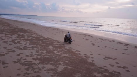 Drone-view-of-a-motorcycle-riding-on-the-beach-with-the-sun-going-down