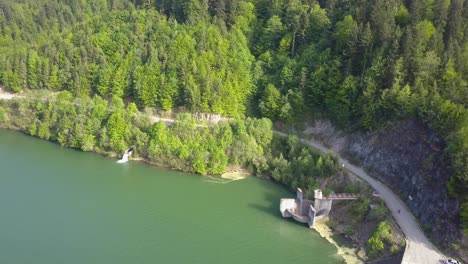Aerial-Downwards-shot-of-road-next-to-lake-reservoir-with-trees-next-to-water-front