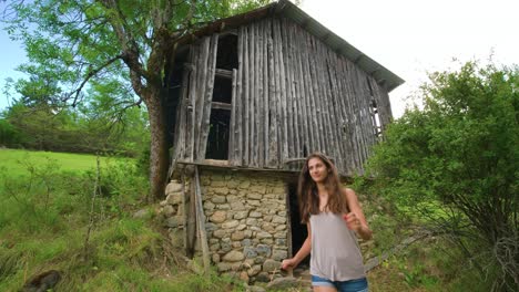A-woman-walks-out-of-an-old-abandoned-stone-shack-in-the-middle-of-a-forest-and-continues-on-her-way