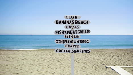 A-sign-at-a-tropical-sandy-beach-showing-directions-for-different-places-for-food-and-drinks
