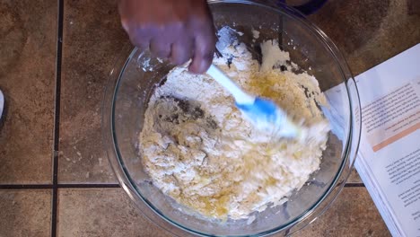 Mixing-flour-and-egg-batter-with-spatula-in-home-kitchen,-Overhead-Close-Up