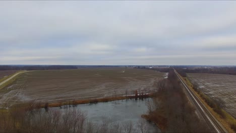 Cars,-trucks-and-a-bus-traveling-across-an-overpass-running-over-railroad-tracks-next-to-a-pond-on-a-rural-Illinois-highway