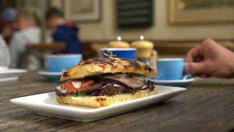SLOWMO---Beef-sandwich-for-breakfast-and-coffees-in-background-in-stylish-cafe