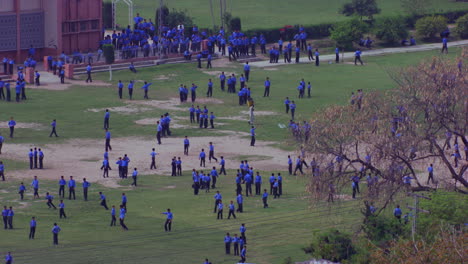School-students-playing-in-the-ground-aerial-view-with-trees,-some-running-and-having-fun,-students-are-in-blue-pants-and-shirts,-some-part-is-missing-of-grass-in-the-ground