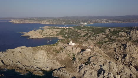 Drohnenaufnahme-Umkreist-Einen-Kleinen-Weißen-Leuchtturm-Auf-Einer-Wilden-Und-Felsigen-Klippe-Im-Norden-Sardiniens