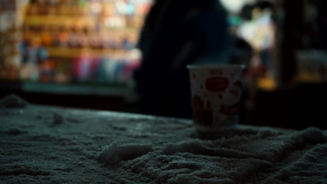 Styrofoam-cup-on-snowy-table-with-people-passing-by-in-the-background