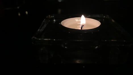 Romantic-slow-motion-of-tea-candle-on-glass-table-at-night-with-glow-and-reflection