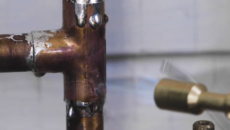 Extreme-closeup-of-a-copper-tee-pipe-being-soldered-during-a-DIY-home-repair