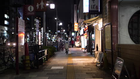 Statische-Aufnahme-Einer-Frau,-Die-Nachts-An-Einem-Frühlingstag-In-Tokio,-Japan,-Auf-Einer-Ruhigen-Straße-Radelt
