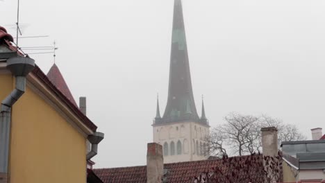 St.-Olaf-Kirche-In-Der-Altstadt-Von-Tallinn,-Von-Den-Straßen-Aus-Gesehen,-Mit-Gelbem-Gebäude-Im-Vordergrund-An-Einem-Nebligen-Wintertag