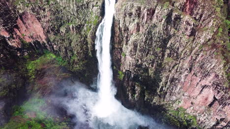 Drone-flying-towards-huge-waterfall,-camera-tilts-down-for-amazing-perspective