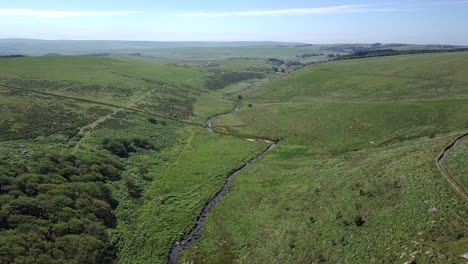 Wide-aerial-shot-tracking-forwards-and-down,-with-wistmans-wood,-a-river-and-grassy-moorland-setting-the-scene