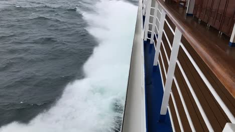 Slow-motion-view-of-the-spraying-water-off-the-left,-port-side-of-a-ship-as-it-hits-the-waves,-lifting-up,-forward-to-the-horizon