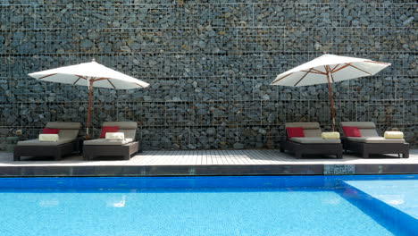 Luxuriöse-Liegestühle-Am-Pool-Mit-Sonnenschirmen-Und-Kristallblauem-Wasser-In-Einem-Tropischen-Resort