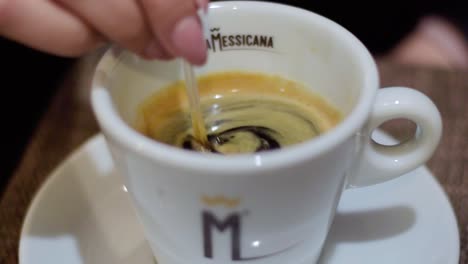 Hand-Einer-Dame,-Die-Im-Restaurant-Zucker-In-Einer-Weißen-Tasse-Starken-Espresso-Mischt