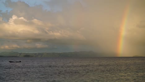 Ein-Regenbogen-Im-Hintergrund,-Während-Ein-Traditionelles-Kleines-Holzboot-Aus-Dem-Bild-Fährt
